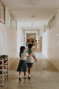 Two children in school uniforms walk through a bright school hallway.